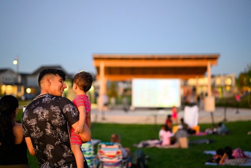 A man holds a young child in his arms at movie night in Reed’s Crossing Park.