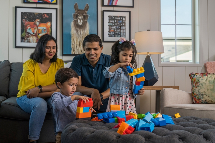 A family with two small children plays with colorful blocks in a living room at Reed’s Crossing.