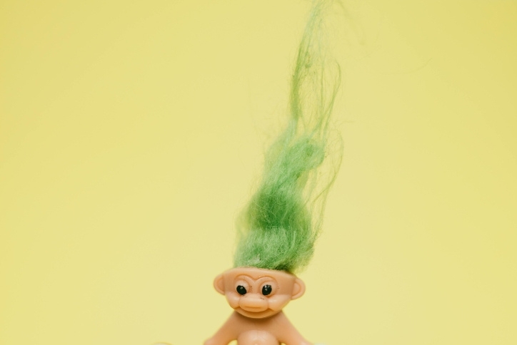 Photo of a troll doll with green hair on a yellow background.