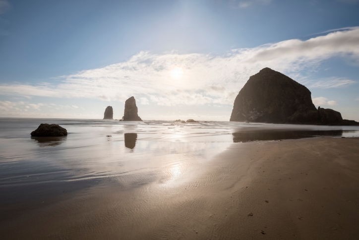 Sun sets behind the iconic rocks on the shore at Cannon Beach, Oregon.