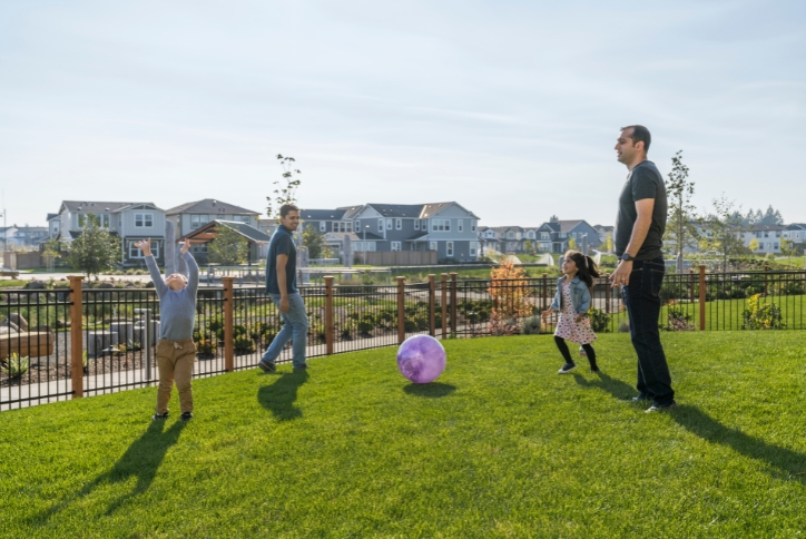 Two adults and two children play with a pink inflatable ball on a grassy lawn.