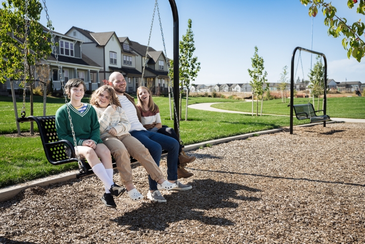 Mother, father, and two teenage girls sit together on a bench swing in Tamarack Park.