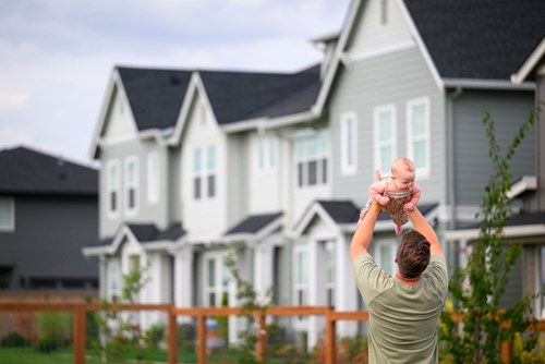 A man holds a laughing baby up over his head in the Reed’s Crossing Community Garden.