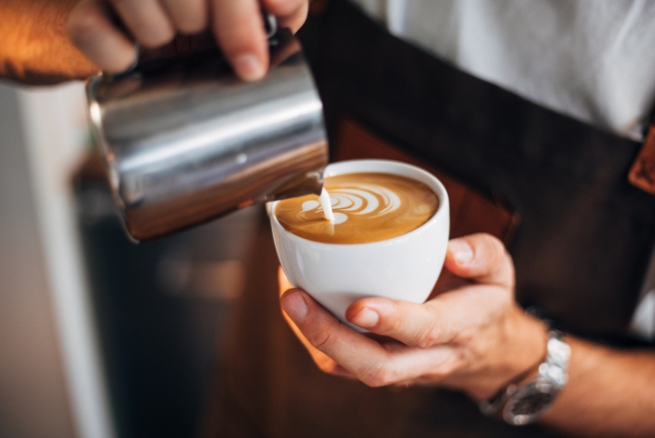 Close-up of a barista pouring milk into coffee to create latte art.